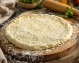 Pâte à pizza prête à être garnie, issue d'une recette de pâte à pizza levure boulanger. La farine est saupoudrée sur la planche en bois.