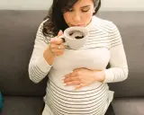 Schwangere Frau trinkt eine Tasse entkoffeinierten Kaffee, während sie ihren Bauch streichelt.