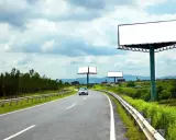 Pusta reklama przy drodze na terenie prywatnym, z widokiem na zakrzywioną autostradę i zielone wzgórza.