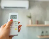 Mano con control remoto de aire acondicionado, ajustando el modo dry para dormir. La pantalla muestra 25°C.