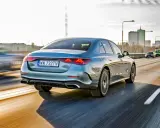 Elegancki, błękitny Mercedes E220d 4MATIC pędzi autostradą, mijając miejską panoramę.
