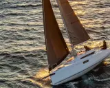 Voilier blanc naviguant sur une mer agitée au coucher du soleil. Les voiles sombres captent la lumière dorée. Idéal pour les premières 30 fiches techniques.