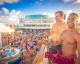 Two men smile on a cruise deck, surrounded by a lively crowd enjoying a pool party. These scenes are typical of positive gay cruises reviews.