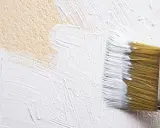 Un pinceau applique de la peinture blanche sur un mur texturé, comme une pierre de chaux.