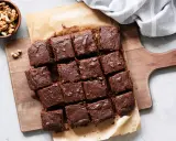 Brownies au chocolat coupés en carrés sur une planche en bois, accompagnés de noix. Un délicieux dessert healthy.