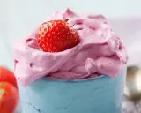 Puszysty, różowy krem z mascarpone z truskawką na wierzchu, podany w niebieskim naczyniu.
