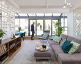 Nowoczesna aranżacja mieszkania 50m2 w bloku. Jasny salon z przeszklonym dachem, szara kanapa, stolik kawowy, regał z książkami i roślinami.