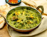 Ein köstliches Palak Paneer in einer traditionellen Schüssel, serviert mit Fladenbrot und Gewürzen.