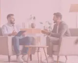 Rozmowa dwóch mężczyzn w przytulnym gabinecie. Jeden z nich, trzymający teczkę, wydaje się wyjaśniać, jak zostać terapeutą uzależnień.