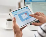 Ręce trzymają tablet z ekranem poczty e-mail, gdzie widać powiadomienie o nowej wiadomości. Może to być początek pisania reklamacji po angielsku.