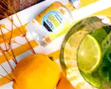 Erfrischende Vodka Cocktails mit Zitrone, Minze und Limette. Eine kleine Flasche Lemon Wodka liegt neben frischen Zitronen und gelben Blumen.
