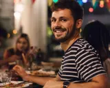 Uśmiechnięty mężczyzna na tle przyjaciół przy stole. Idealny, tani pomysł na wieczór kawalerski z jedzeniem i dobrym towarzystwem.