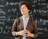 Lehrerin vor Tafel mit Matheformeln. Sie fragt sich, wie viel verdienen Grundschullehrer.