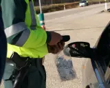 Policjant w kamizelce odblaskowej trzyma alkomat i worek z ustnikami przy samochodzie.