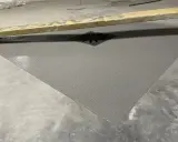 Nowa, szara posadzka w garażu z odpływem. Drewniana łata budowlana leży na jej powierzchni.