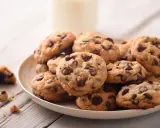 Une assiette de délicieux cookie fait maison, parsemés de pépites de chocolat, avec un verre de lait en arrière-plan.