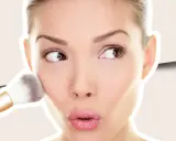 Una mujer aplica colorete en crema en sus mejillas con una brocha, creando un look natural y radiante.