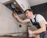 Un homme en salopette utilise un tournevis pour comment installer une hotte de cuisine.