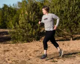 Frau beim **trail running** auf sandigem Untergrund, umgeben von Kiefern und Bäumen.