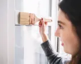 Mujer pintando un marco blanco de PVC con brocha. Aprende como pintar PVC para renovar tus espacios.