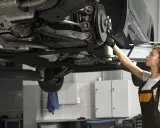 Mechaniczka sprawdza układ napędowy samochodu na podnośniku.