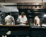 Chefs in a professional kitchen, one plating food.