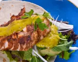 Delicioso wrap de pollo con aguacate, lechugas variadas y salsa verde, servido en un plato azul vibrante.