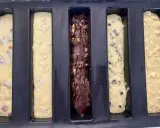Cinq moules à cake longs prêts pour la cuisson : un aux fruits rouges, un aux amandes, un au chocolat, un aux pépites de chocolat et un aux pommes. Recette 5 cakes longs sucrés.