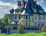 La villa Demoiselle à Reims, une demeure d'exception avec ses toits bleus et ses ornements verts, se dresse fièrement derrière une grille ouvragée.