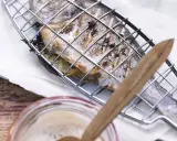 Ein ganzer Fisch liegt in einem Grillkorb, bereit zum Fisch grillen. Zitronenscheiben und Kräuter sind darin versteckt.