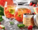 Rafraîchissante recette thé glacé : deux verres remplis de glaçons, fruits rouges et menthe, accompagnés de pastèque et d'une boîte de thé.