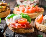 Verschiedene herzhafte Snacks auf geröstetem Brot: Bruschetta mit Tomaten, Pilzen, Schinken und Mozzarella.
