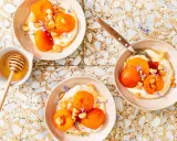 Trois bols de compote abricot onctueuse, garnie d'amandes et de fleurs violettes. Un pot de miel avec sa cuillère est à côté.