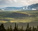 Välkommen till Vålådalens naturreservat! En vidsträckt vy över fjäll, skog och snöfläckar under en dramatisk himmel.