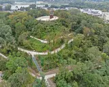 Wzgórze z pomnikiem Kotwicy, otoczone zielenią. Kręte ścieżki i schody prowadzą przez park akcji "Burza", oferując widok na miasto i Wisłę.