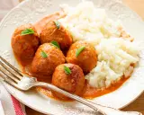 Albondigas a la jardinera con arroz blanco, decoradas con hojas verdes. Un tenedor plateado descansa sobre el plato.
