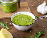 Frisches Rucola Pesto in einer Schüssel, daneben Zitrone, Knoblauch und Rucolablätter.