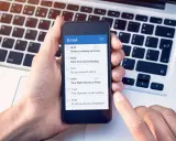 Dłoń trzyma smartfon z listą e-maili, w tym "Your flight tickets to Paris". Kiedyś, yours sincerely, wysłałbym takie wiadomości.