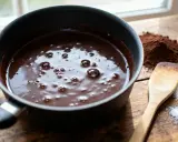 Une casserole de chocolat fondant, avec du cacao en poudre et du sucre à côté, prêt à faire fondre du chocolat pour un dessert gourmand.