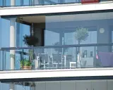 Un balcone moderno con vetrate scorrevoli, ideale per chiudere un balcone fai da te. Tavolo, sedie e un pouf viola creano un angolo relax.