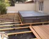 Construction d'une terrasse en bois autour d'un spa. L'espacement des plots sur le plot béton est visible, prêt pour les lames de bois.