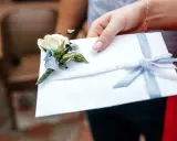 Biała koperta z błękitną wstążką i butonierką, symbolizująca pieniądze z wesela na konto.