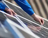 Händer i blå arbetskläder monterar solpaneler från Longi Solar på ett tak.
