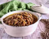 Un invitante piatto di lenticchie in umido, servito in una ciotola rustica, con un panno verde sullo sfondo.