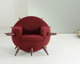 A round, burgundy armchair with pointed legs and armrests, in a minimalist room.