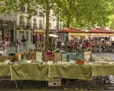 Ein Buchstand mit alten Büchern auf einem sonnigen Platz in Rennes, Frankreich. Im Hintergrund sitzen Menschen in einem Straßencafé.