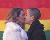 Deux femmes s'embrassent tendrement devant un drapeau arc-en-ciel, une belle représentation de l'amour saphique.
