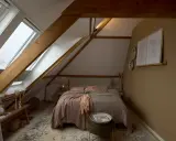 Przytulna sypialnia na bardzo niskim poddaszu użytkowym. Drewniane belki, okna dachowe i ciepłe kolory tworzą przytulną atmosferę.