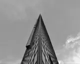 Minimalistyczne fotografowanie architektury. Ostry szczyt wieżowca przecina niebo, odbijając chmury w szklanej fasadzie.