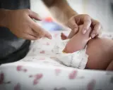 Ojciec zmienia pieluchę, na której widać, co to jest kupa. Dziecko leży na przewijaku z flamingami.